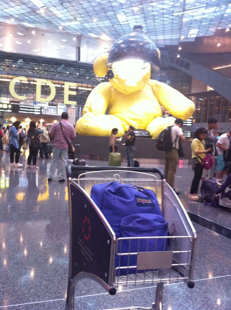 Picture of my purple backpack in front of the Giant Bear of Doha Airport